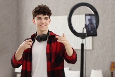 Photo of Smiling teenage blogger pointing at his smartphone while streaming at home