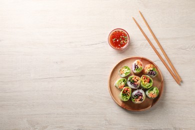 Photo of Tasty spring rolls, chopsticks and sauce on white wooden table, flat lay. Space for text