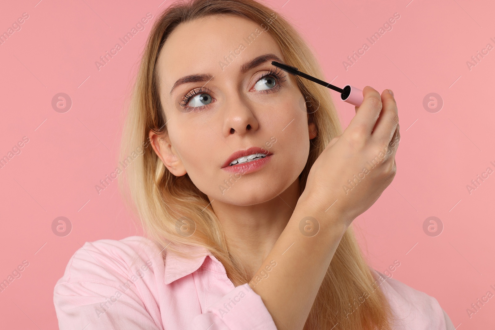 Photo of Beautiful woman applying mascara on pink background, closeup