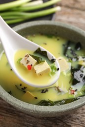 Delicious miso soup with tofu in spoon above bowl, closeup