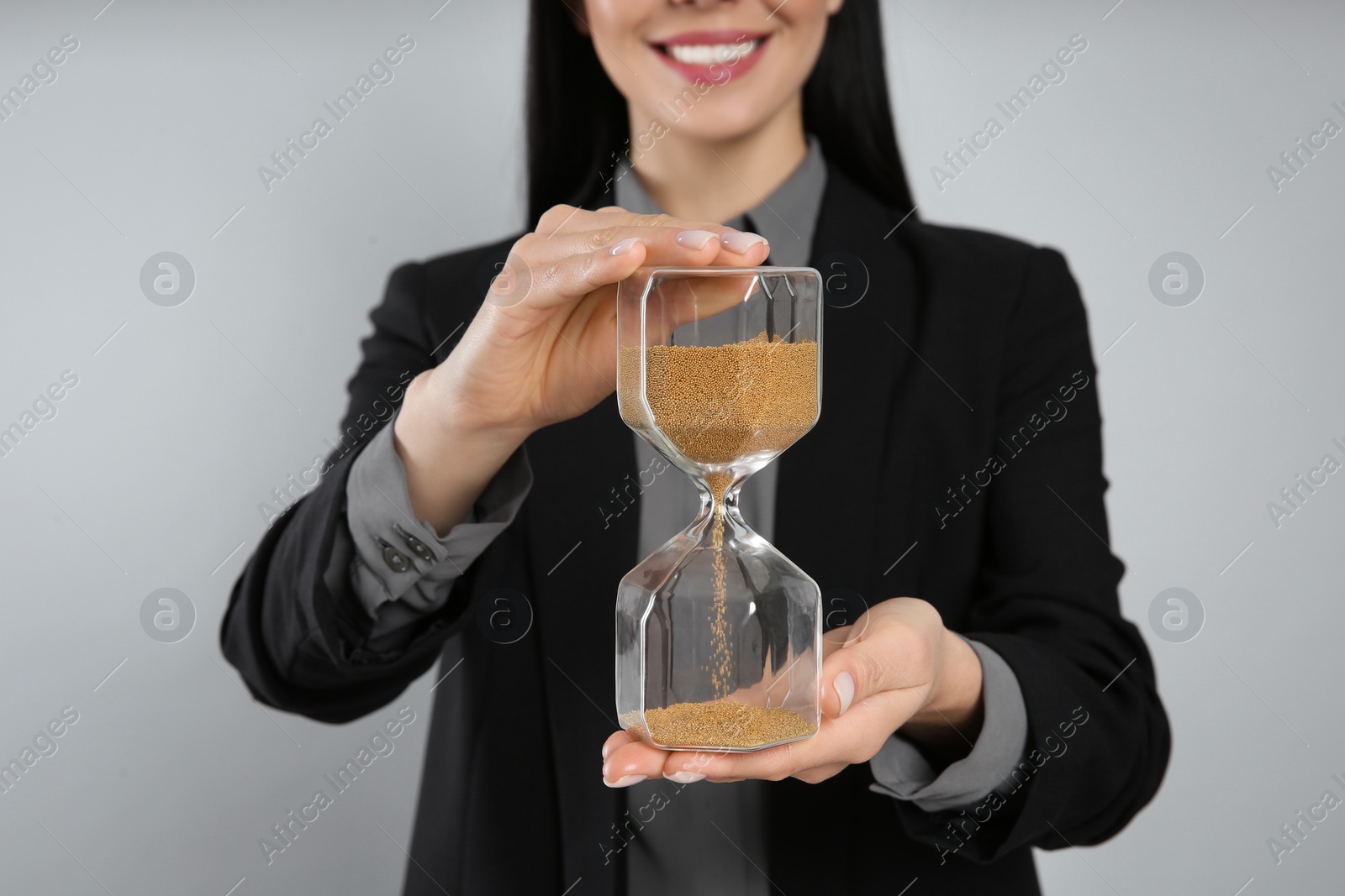 Photo of Businesswoman holding hourglass on light grey background, closeup. Time management