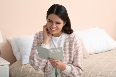 Photo of Young woman with greeting card on bed in room, space for text