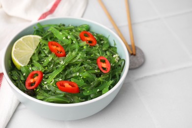 Photo of Tasty seaweed salad in bowl served on white tiled table, closeup