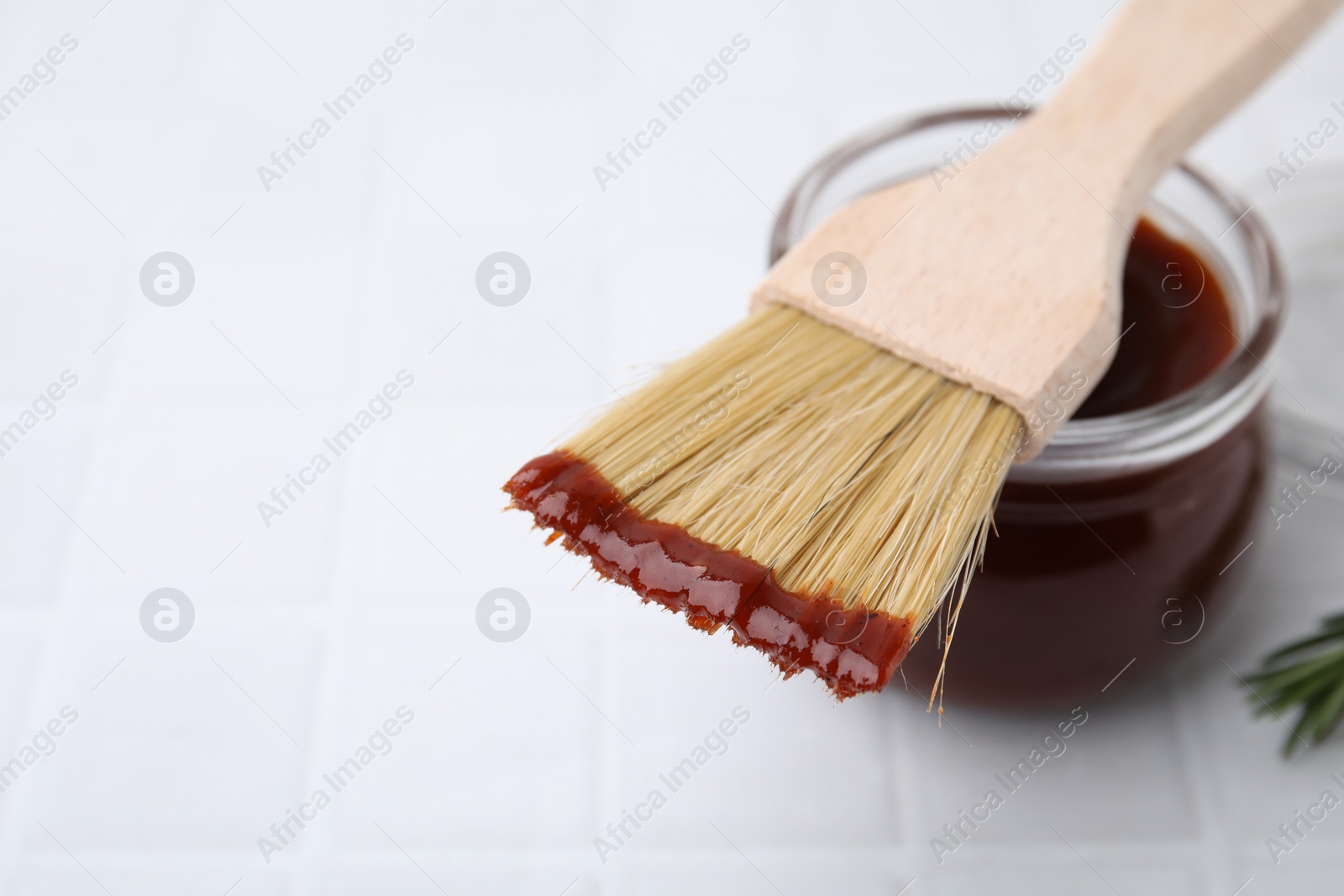 Photo of Marinade in jar and basting brush on white tiled table, closeup. Space for text