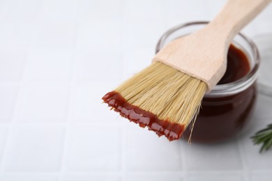 Marinade in jar and basting brush on white tiled table, closeup. Space for text