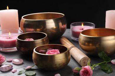 Photo of Tibetan singing bowls with beautiful rose flowers, mallet and burning candles on gray table