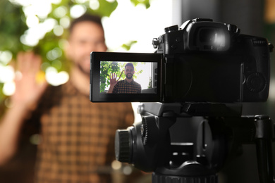 Young blogger recording video indoors, focus on camera screen