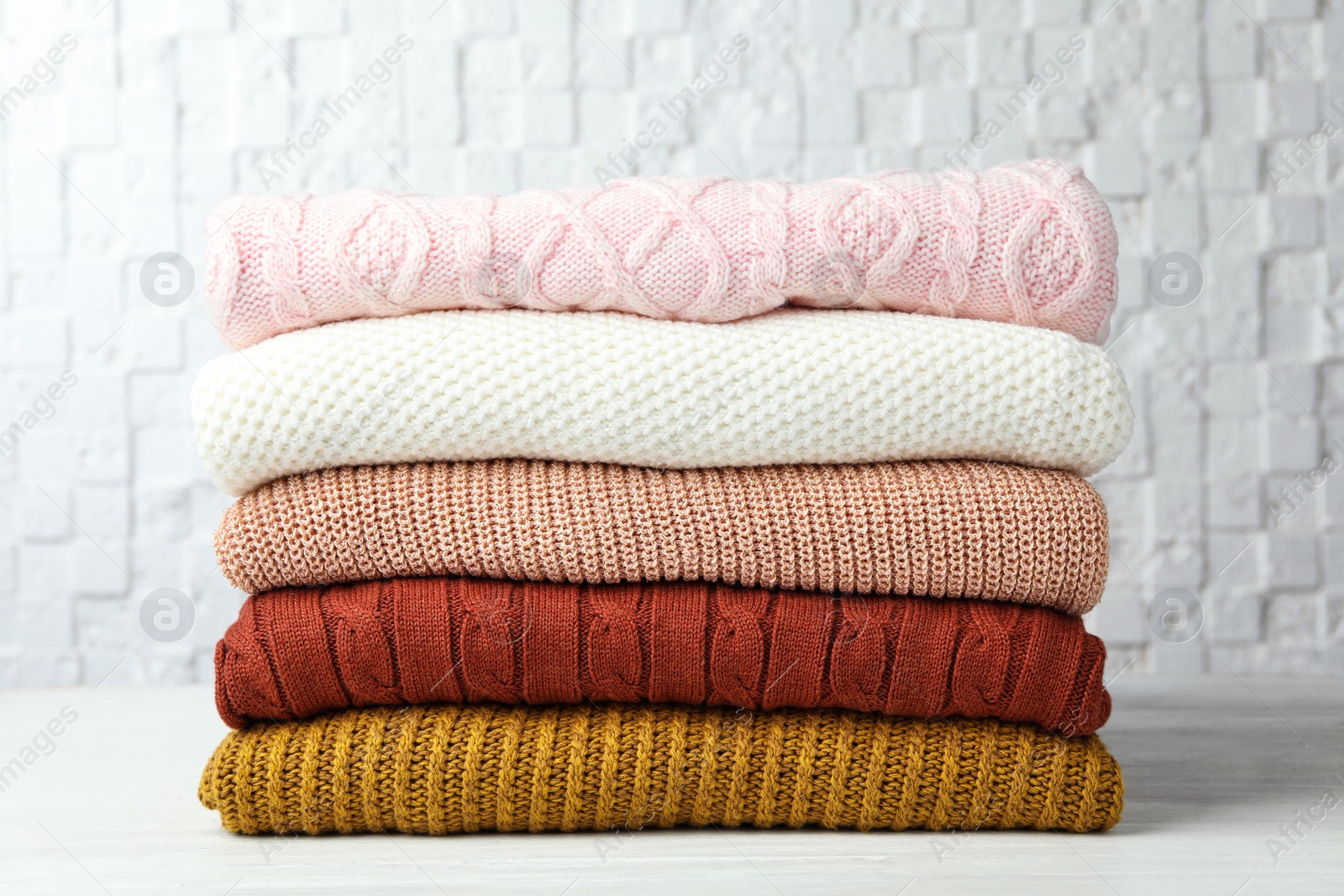 Photo of Stack of warm clothes on white wooden table against textured wall. Autumn season