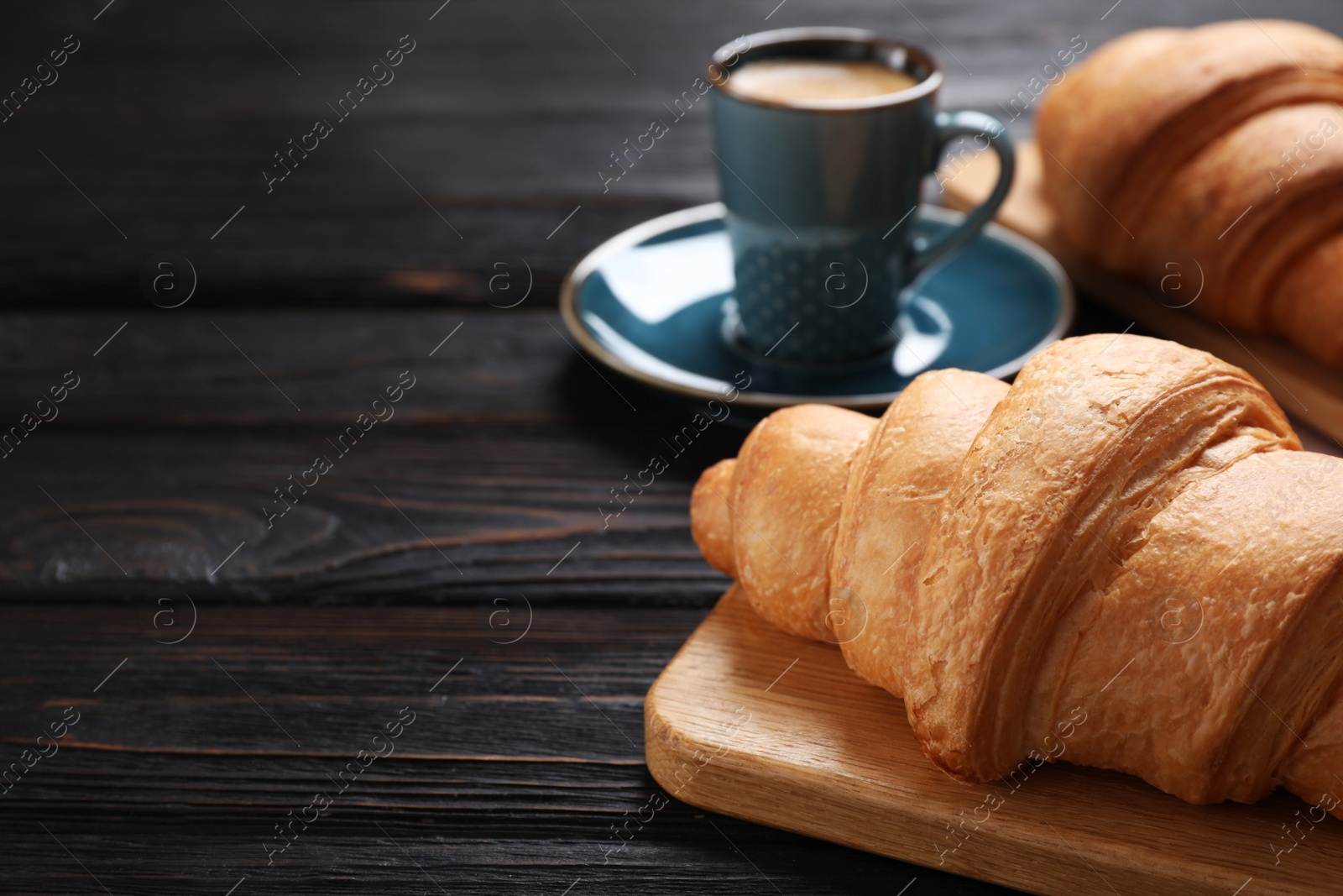 Photo of Tasty fresh croissants and coffee on black wooden table, closeup. Space for text