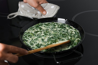 Woman cooking tasty spinach dip on kitchen stove, closeup view