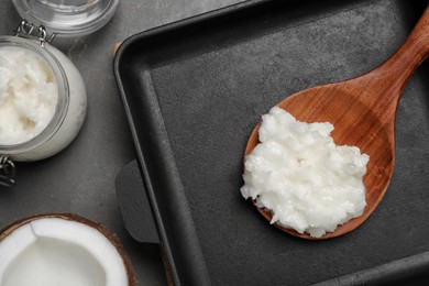 Photo of Baking dish with coconut oil and wooden spoon on grey table, flat lay