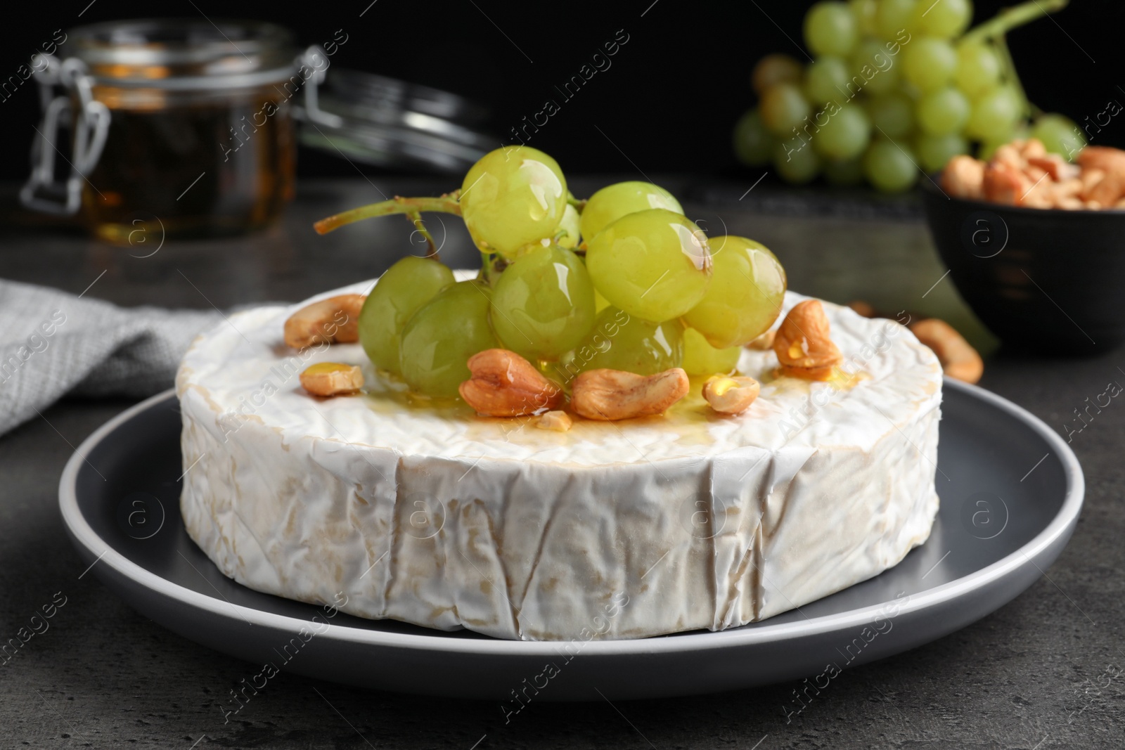 Photo of Brie cheese served with grape, cashew nuts and honey on dark grey table, closeup