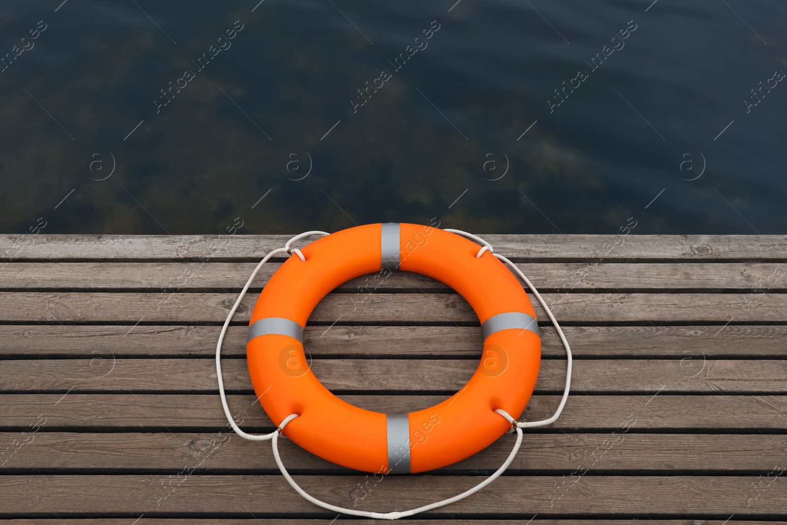 Photo of Orange lifebuoy on wooden pier near water. Rescue equipment