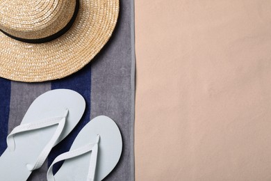 Beach towel, hat and flip flops on sand, flat lay. Space for text