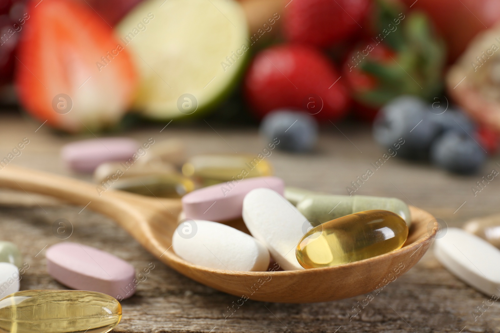 Photo of Different vitamin pills in spoon on wooden table, closeup