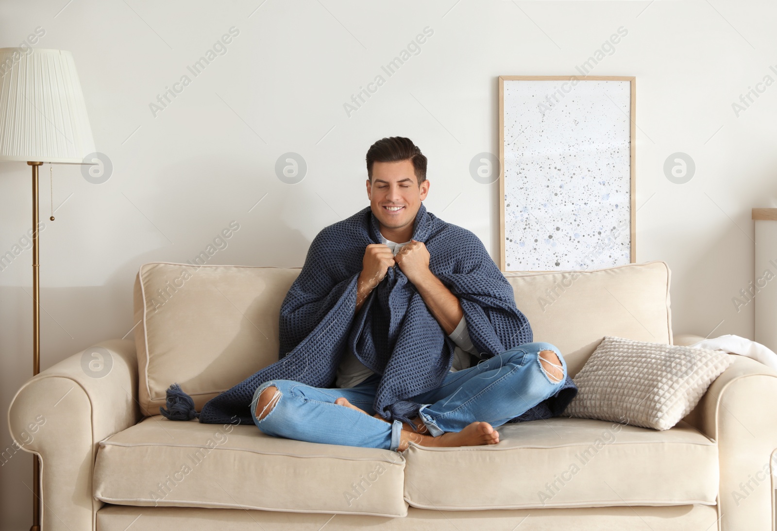 Photo of Man covered with warm dark blue plaid sitting on sofa at home