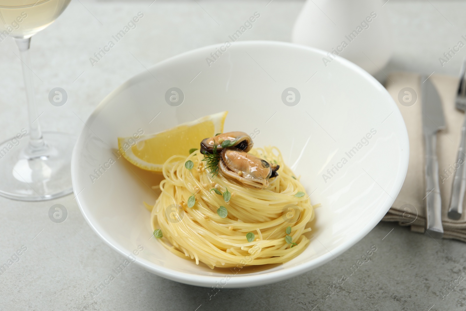 Photo of Tasty capellini with mussels and lemon served on light grey table, closeup. Exquisite presentation of pasta dish