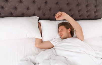 Photo of Handsome young man stretching while lying under blanket, view from above. Bedtime