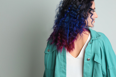 Photo of Young woman with bright dyed hair on grey background, back view. Space for text