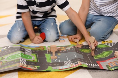 Photo of Little children playing with set of wooden road signs and toy cars indoors, closeup
