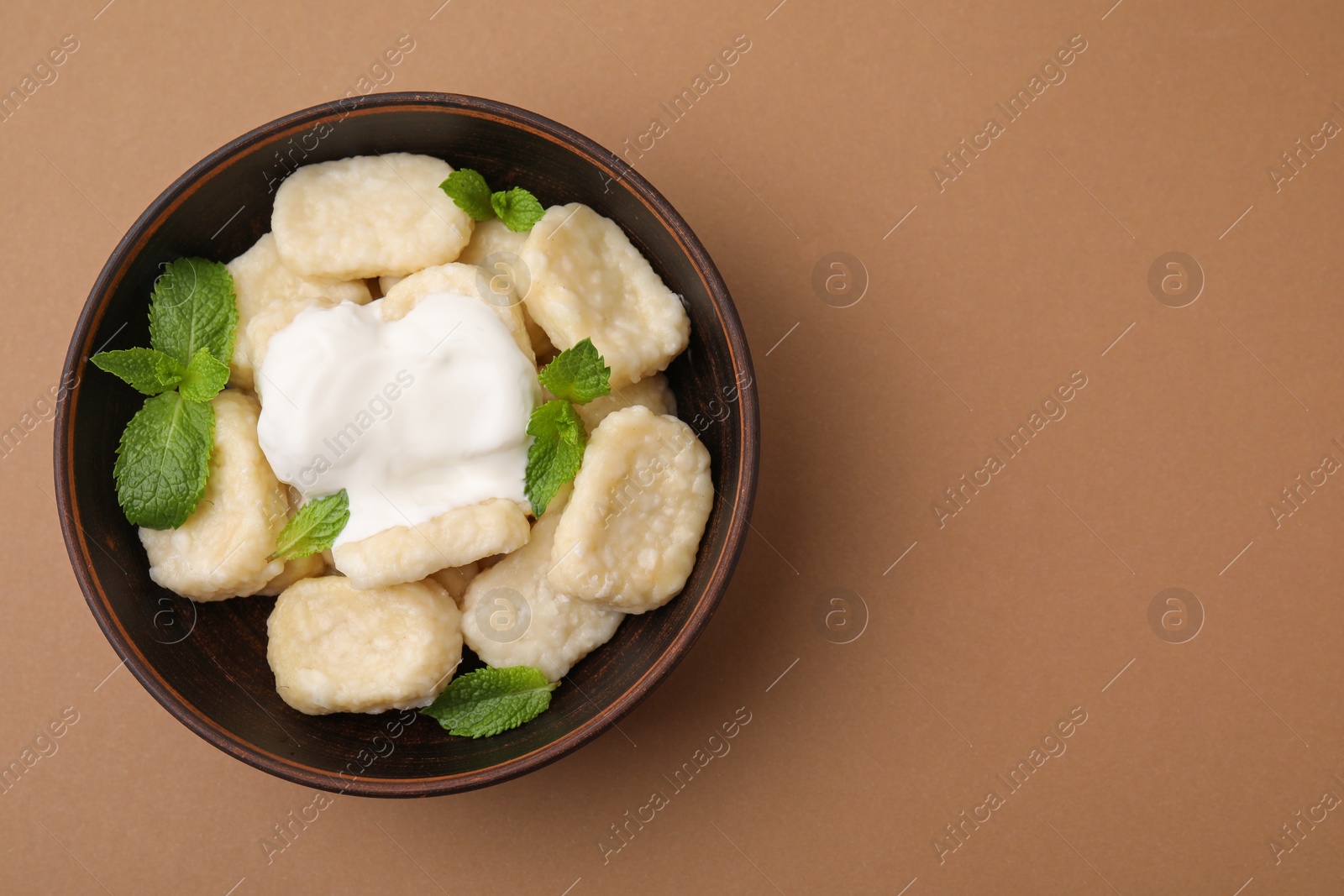 Photo of Bowl of tasty lazy dumplings with sour cream and mint leaves on light brown background, top view. Space for text