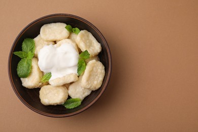 Bowl of tasty lazy dumplings with sour cream and mint leaves on light brown background, top view. Space for text