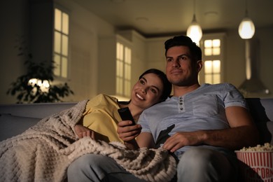 Photo of Couple watching movie with popcorn on sofa at night