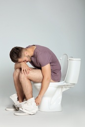Photo of Young man suffering from diarrhea on toilet bowl against gray background