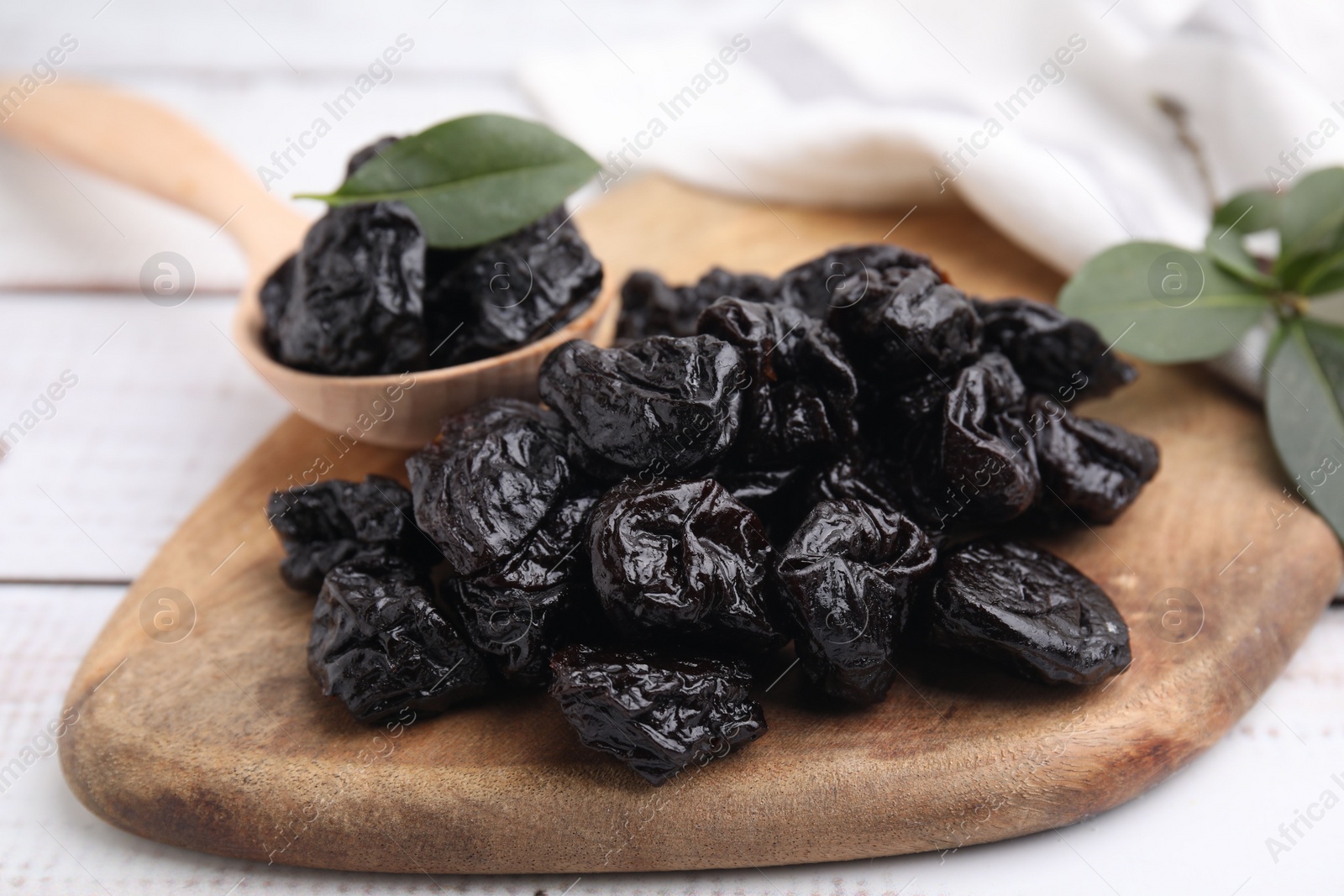 Photo of Spoon with tasty dried prunes and green leaves on light wooden table, closeup