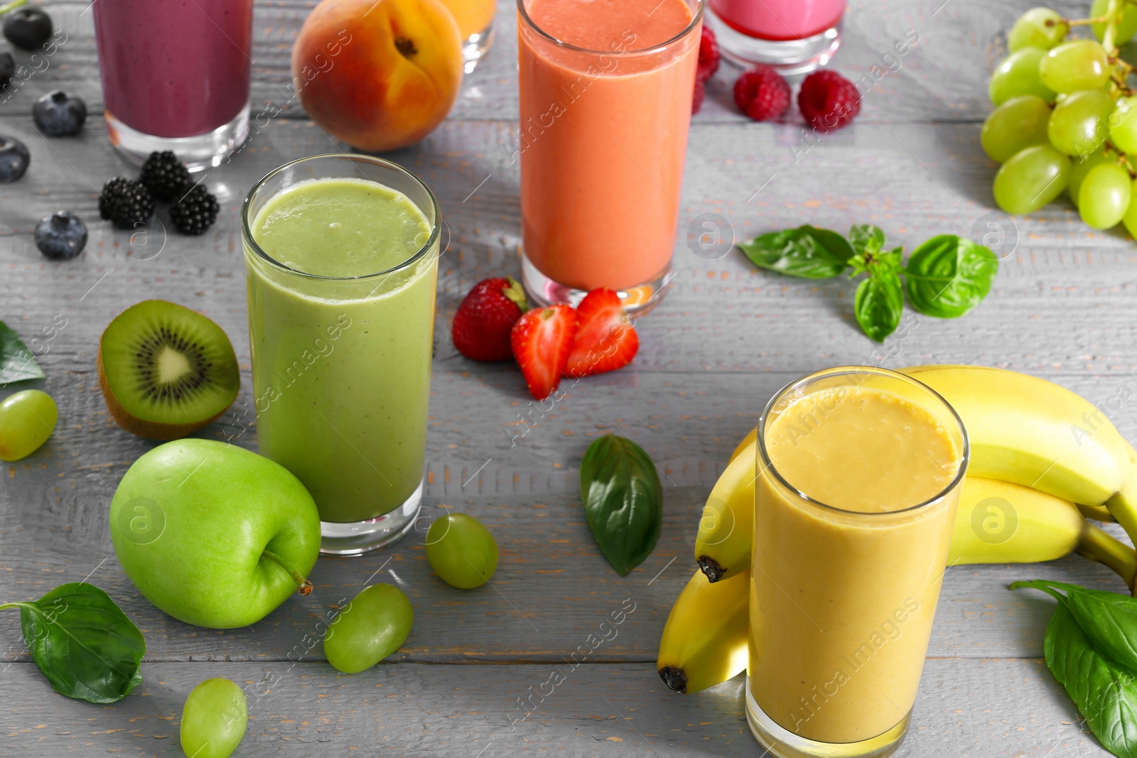 Photo of Many different delicious smoothies and ingredients on grey wooden table