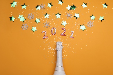 Photo of Year number 2021, champagne bottle and shiny confetti on orange background, flat lay