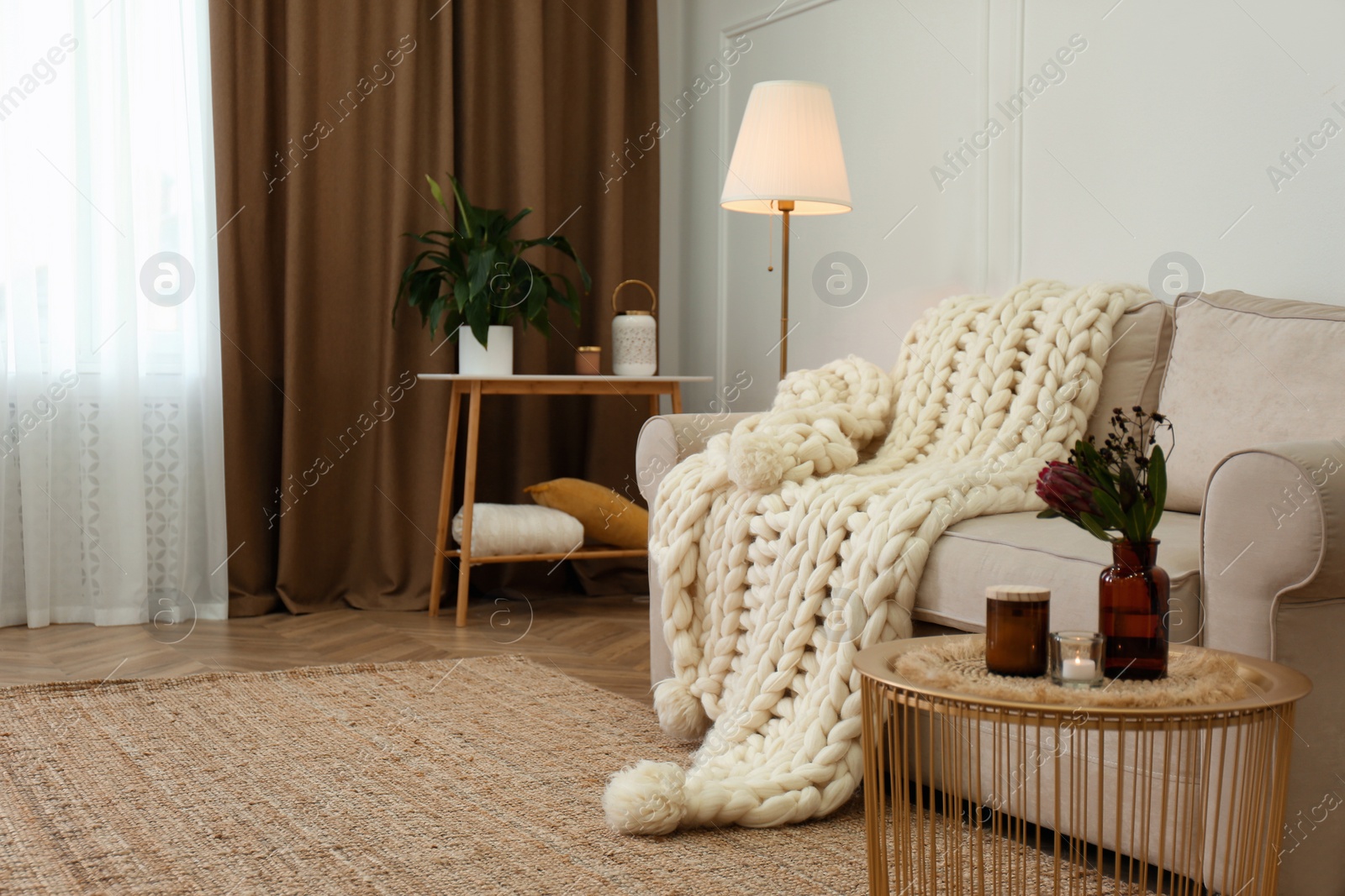 Photo of Soft knitted blanket on couch in living room. Interior element