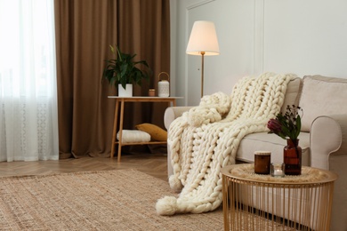 Photo of Soft knitted blanket on couch in living room. Interior element