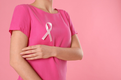 Woman with pink ribbon on color background, closeup. Breast cancer awareness