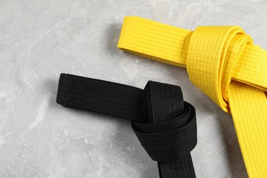 Photo of Black and yellow karate belts on gray marble background, flat lay