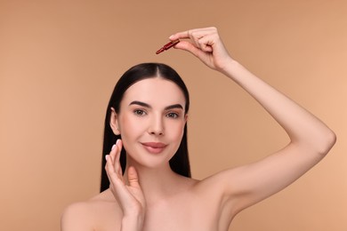 Beautiful young woman using ampoule for hair treatment on beige background