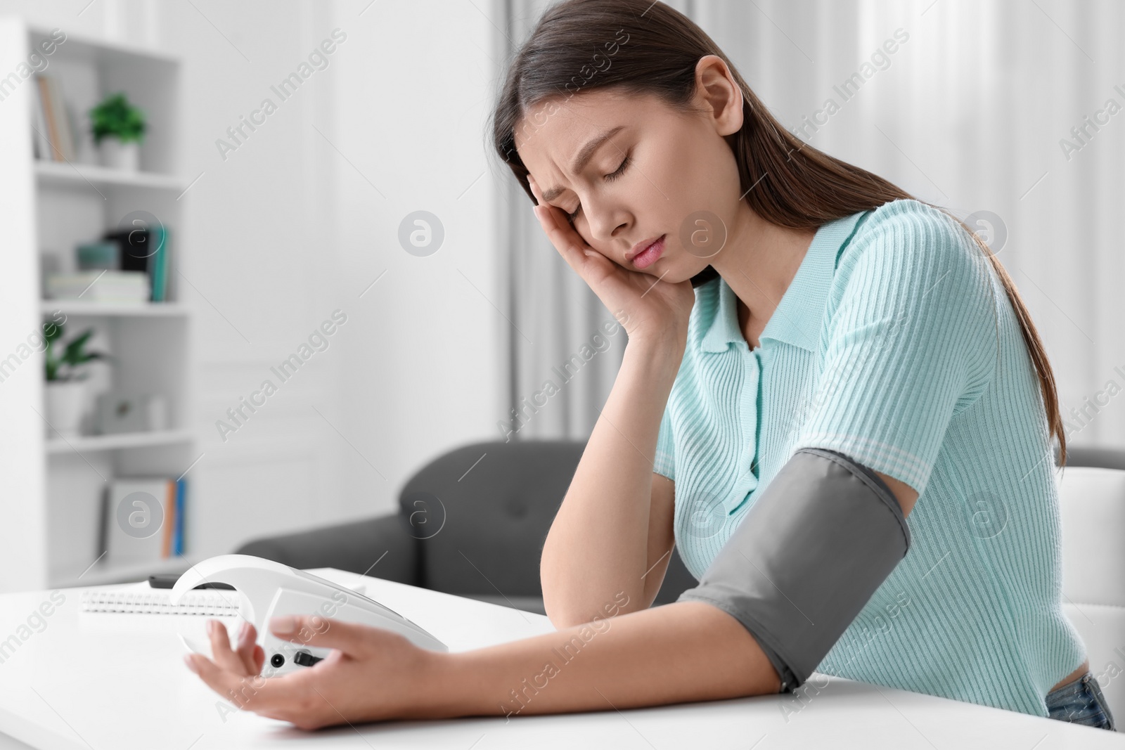 Photo of Woman suffering from headache and measuring blood pressure with tonometer at home