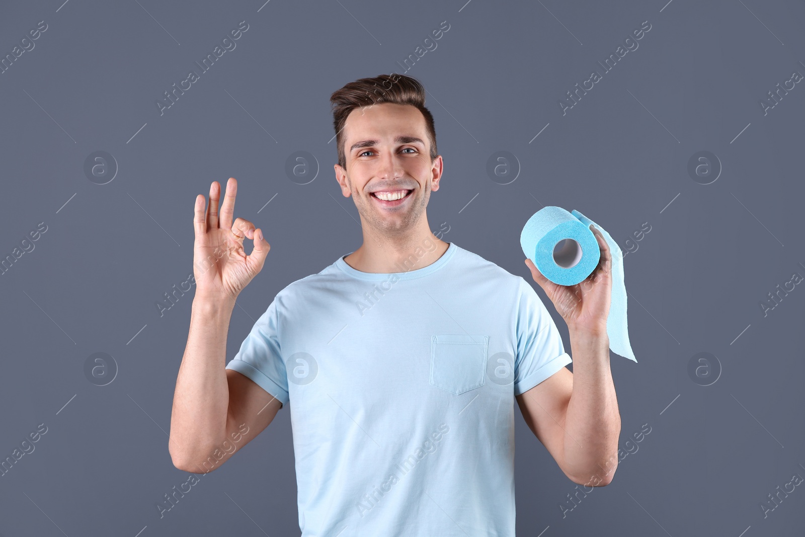 Photo of Young man holding toilet paper roll on color background