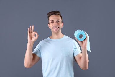 Photo of Young man holding toilet paper roll on color background