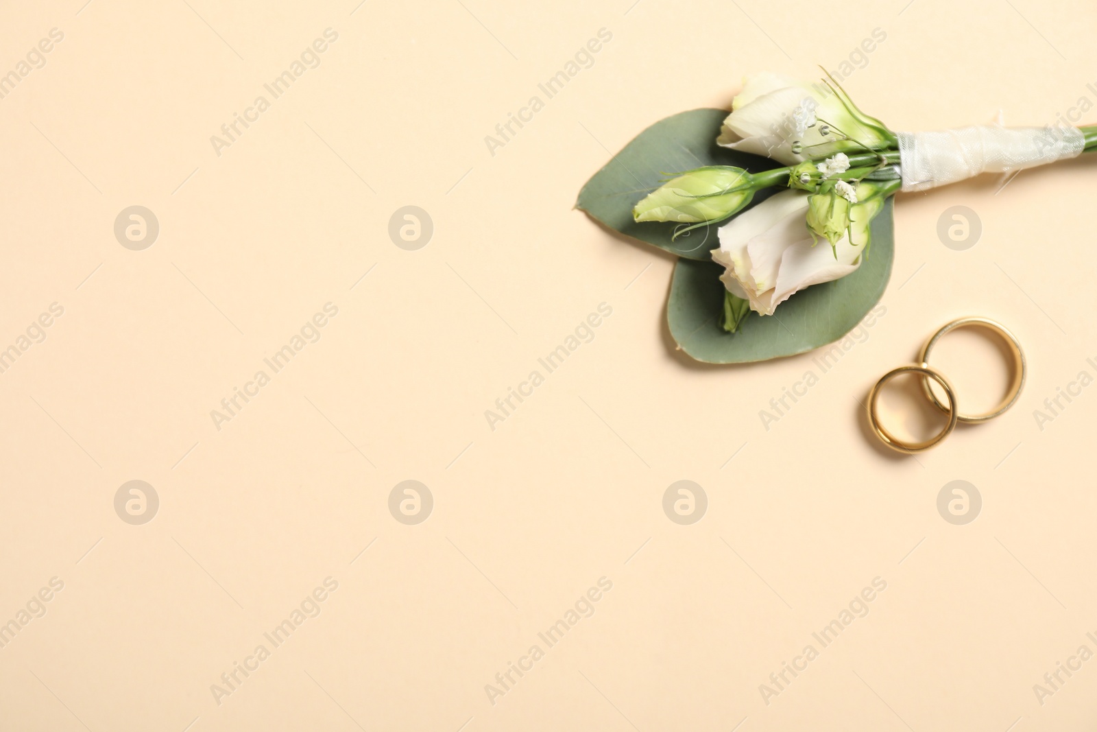 Photo of Wedding stuff. Stylish boutonniere and rings on beige background, top view. Space for text
