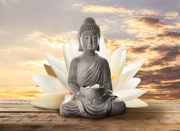 Image of Beautiful stone Buddha sculpture with flower petals on wooden surface at sunset 