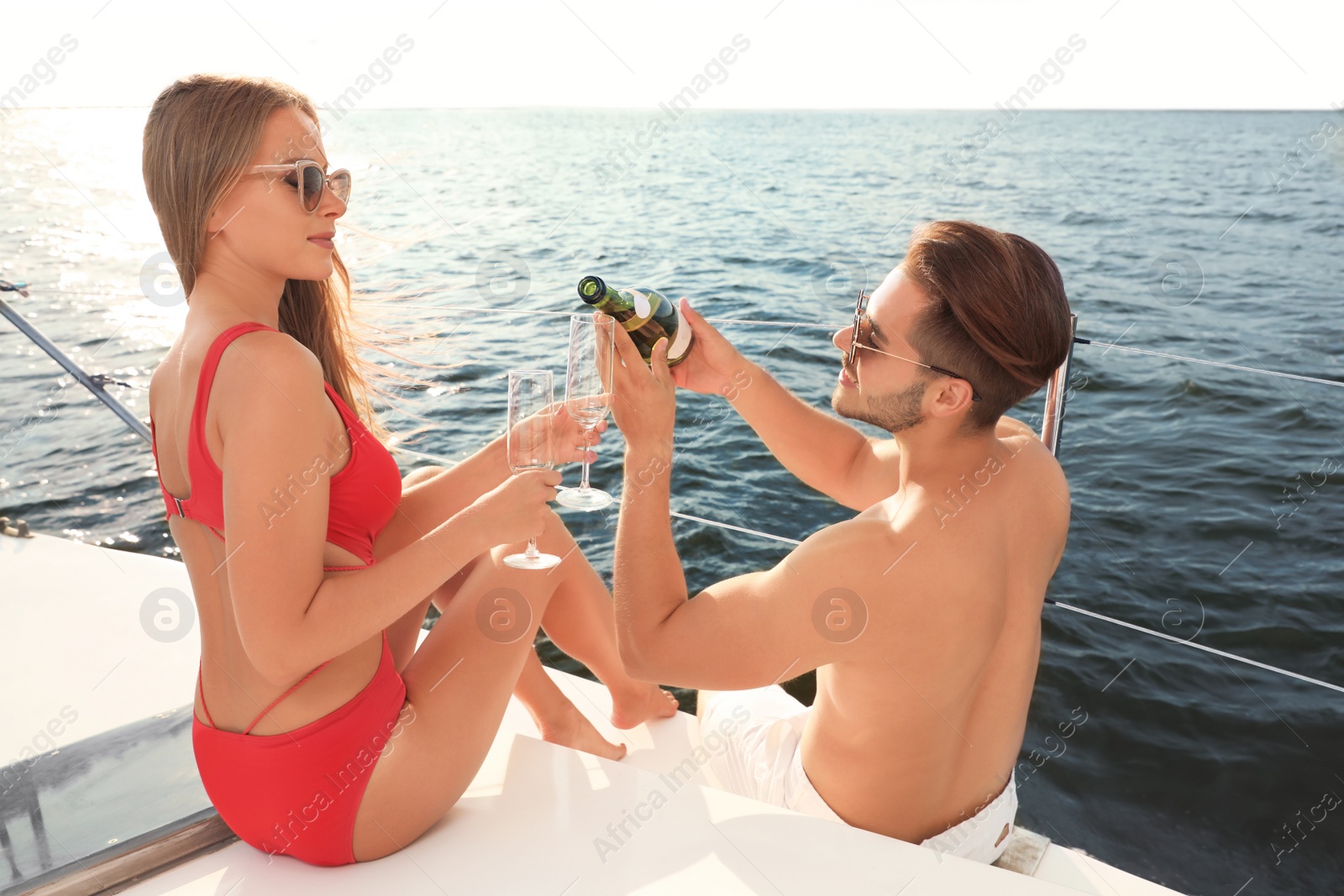 Photo of Young man and his girlfriend in bikini drinking champagne on yacht. Happy couple on vacation