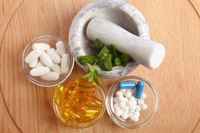 Photo of Mortar with fresh mint and pills in bowls on wooden board