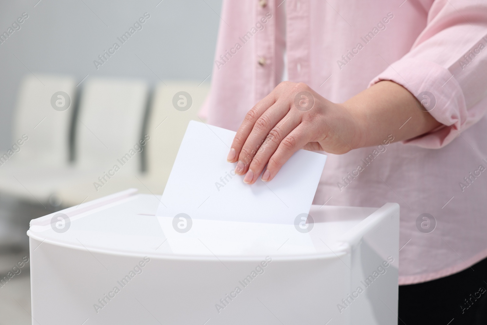 Photo of Woman putting her vote into ballot box on blurred background, closeup