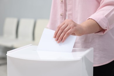 Photo of Woman putting her vote into ballot box on blurred background, closeup