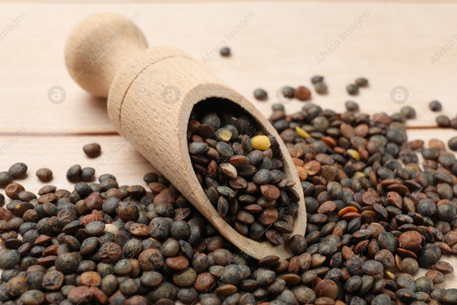Photo of Scoop and many raw lentils on light wooden table, closeup
