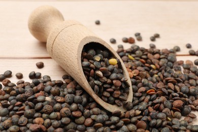 Scoop and many raw lentils on light wooden table, closeup