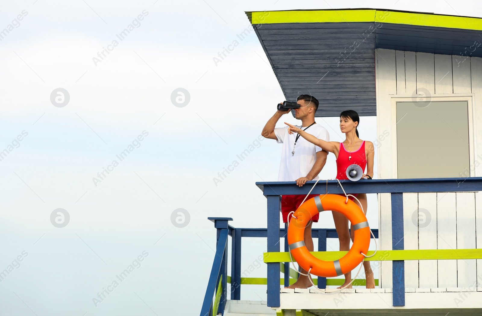 Photo of Lifeguards with megaphone and binocular on watch tower against blue sky