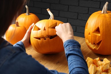 Woman carving pumpkin at wooden table, closeup. Halloween celebration