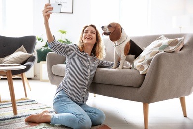 Photo of Young woman taking selfie with her dog at home